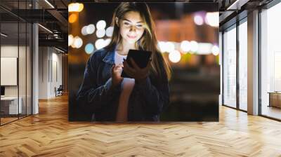 Beautiful young woman using tablet in the city at night bokeh Wall mural